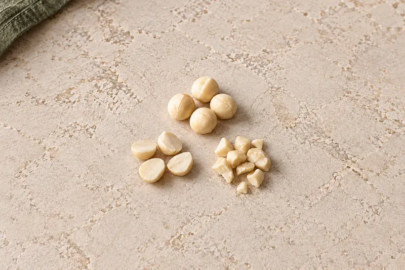 AI-generated photograph-style comparison of whole macadamia kernels above, kernel halves at lower left and irregular kernel pieces at lower right.