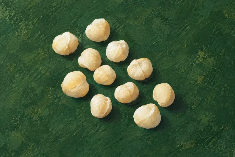 Painted ivory macadamia kernels scattered loosely on dark green textured paper; conceptual food-form context, not a measured lot.
